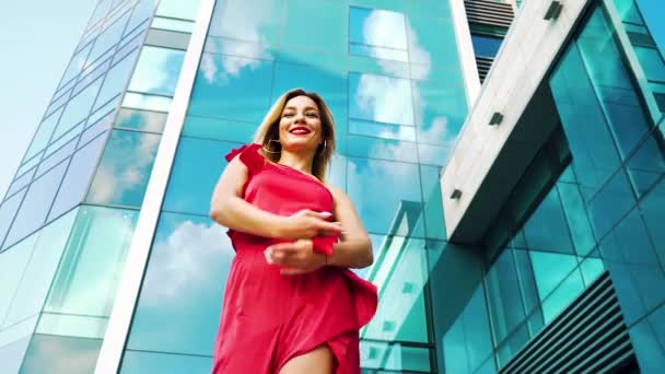 Lage hoek van jonge dame dansen in de richting van bewegende camera met wolkenkrabber achter haar — Stockvideo