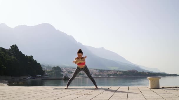 Fit girl flexión en yoga asana en muelle de mar en hermoso paisaje — Vídeos de Stock