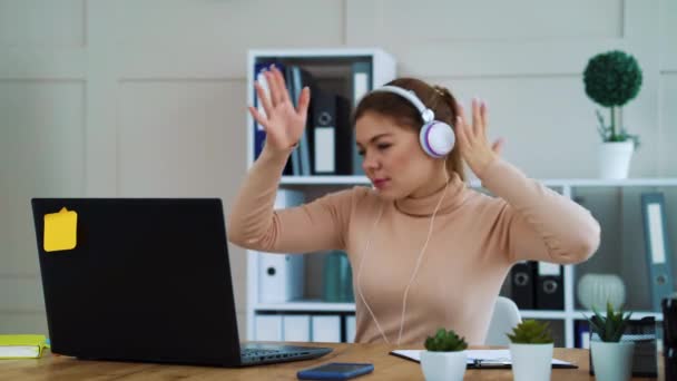 Счастливая работница в наушниках слушает музыку в офисе — стоковое видео