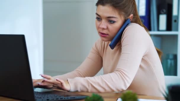 Chica de oficina ocupada hablando por teléfono y escribiendo en el ordenador portátil — Vídeos de Stock