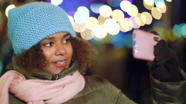 Joyful black girl making funny face for selfie video on Christmas market