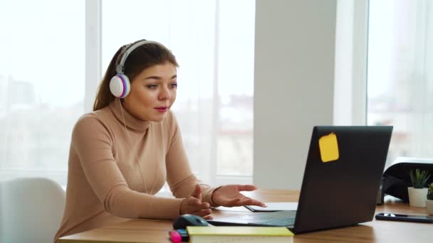 Ragazza allegra in cuffia con videoconferenza sul computer portatile in ufficio — Video Stock