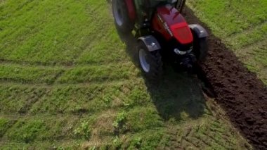aerial of red tractor plowing soil on green agricultural field