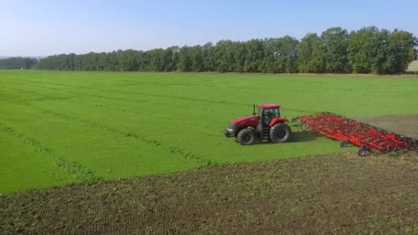 Aerial shot of red tractor plowing agricultural field in summer — ストック動画