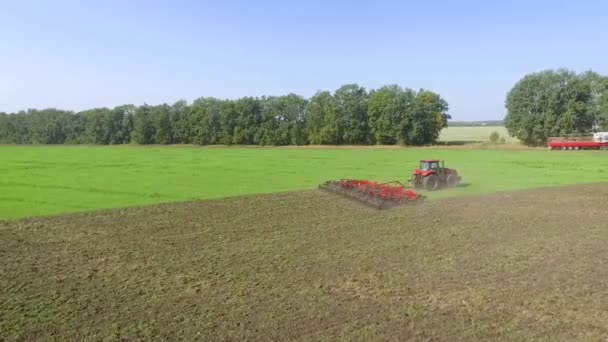 Aerial shot of red tractor cultivating soil on agricultural field — Stockvideo