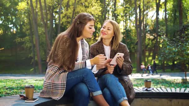 Chicas de moda viendo fotos en las redes sociales utilizando el teléfono inteligente en el parque — Vídeos de Stock