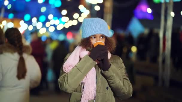 African American girl warming up with hot drink on winter holiday market — ストック動画
