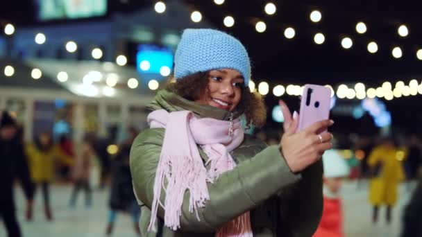 Улыбающаяся черная девушка записывает селфи видео, катаясь на катке ночью — стоковое видео
