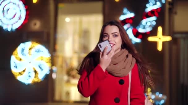 Hermosa chica caminando por la calle decorada con luces y hablando por teléfono — Vídeos de Stock