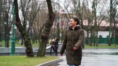 Happy African American girl skipping and dancing in public park in dull weather