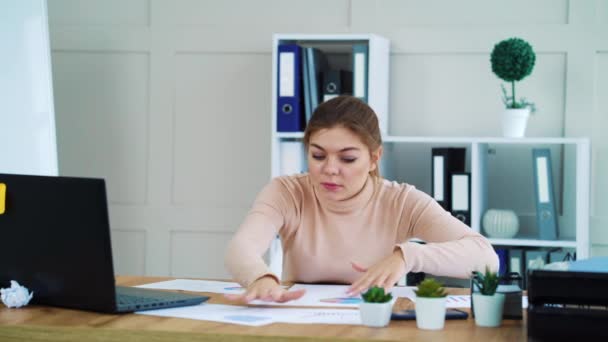Menina do escritório à procura de gráfico necessário entre os papéis na área de trabalho — Vídeo de Stock
