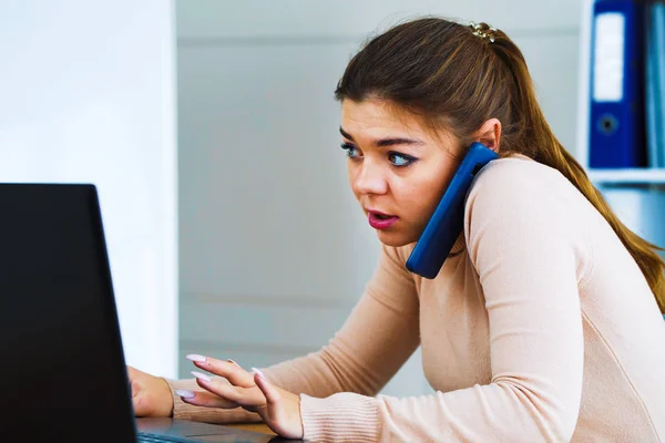 Busy office girl talking on phone and typing on laptop