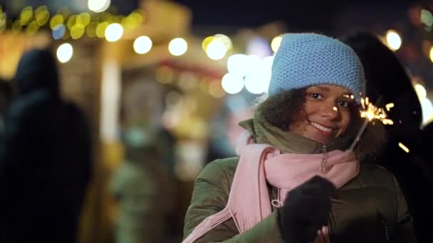 Positive African American girl having fun with sparklers on Christmas market — Stock Video