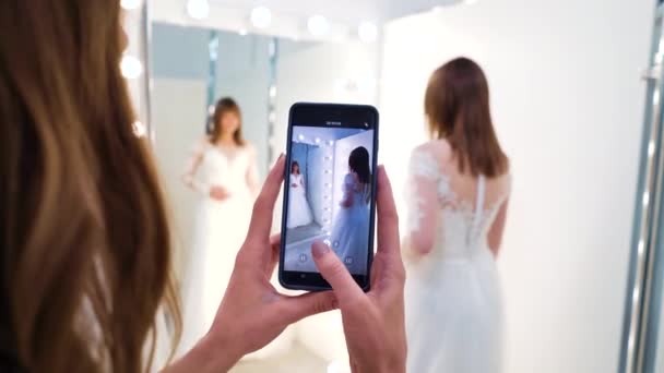 Bruidsmeisje opname video van bruid proberen op trouwjurk in salon — Stockvideo