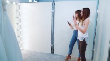 Kızlar kuaförde gelinlik giymiş mutlu gelinin fotoğraflarını çekiyor.