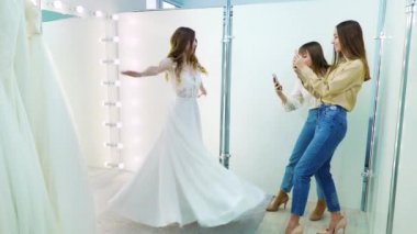 Girls taking photo of happy bride spinning in front of mirror in wedding dress