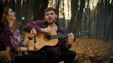 Happy tourists singing songs with guitar in autumn forest