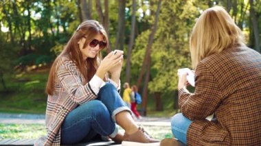 Happy girls browsing photos in social media sitting in green park