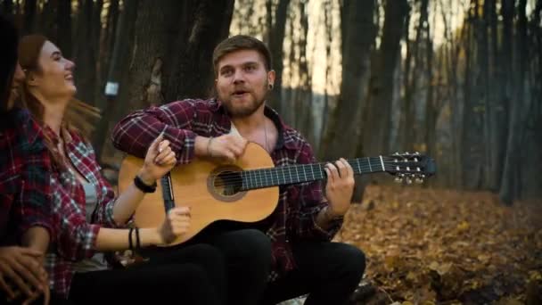 Счастливые туристы поют песни с гитарой в осеннем лесу — стоковое видео