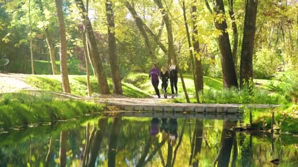 Athletic girls jogging across bridge over river in city park — Stock Video