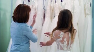 Dressmaker and young bride choosing wedding dresses in salon