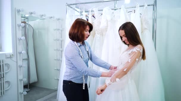 Mujer sastre comprobar vestido de novia en la novia joven en el salón — Vídeos de Stock