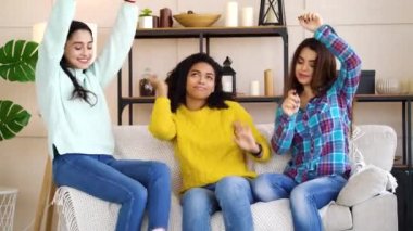 Happy multiracial girls having fun and dancing on sofa at home