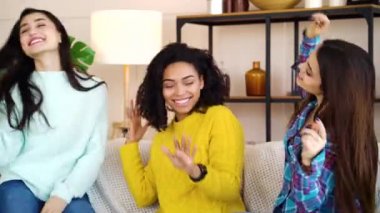 Happy female friends spending time together and dancing on sofa at home