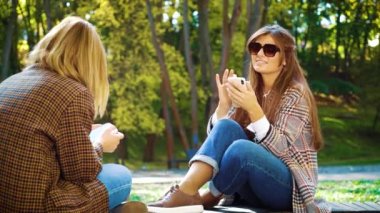 Neşeli kızlar parkta oturup sosyal medyaya bakıyorlar.