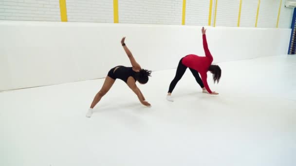 Multiracial girls in sportswear leaning forward and stretching legs in gym — Stock Video