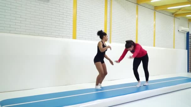 Treinador de ginástica ajudando menina fazendo suporte e salto mortal em tapetes no ginásio — Vídeo de Stock