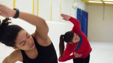 Athletic girls inclining to sides and stretching back and arms in gym