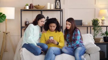 Sad multiracial girls browsing social media on smartphone at home