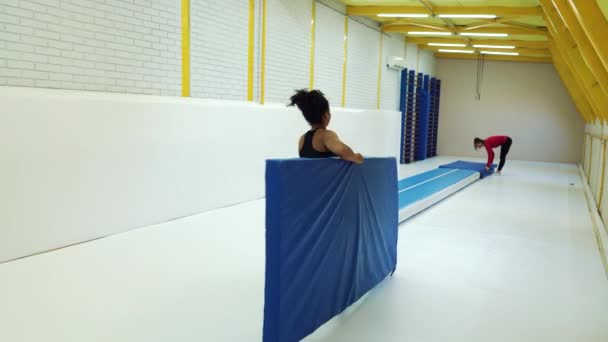 Atletas femeninas preparando alfombras para el entrenamiento de gimnasia en el gimnasio — Vídeos de Stock