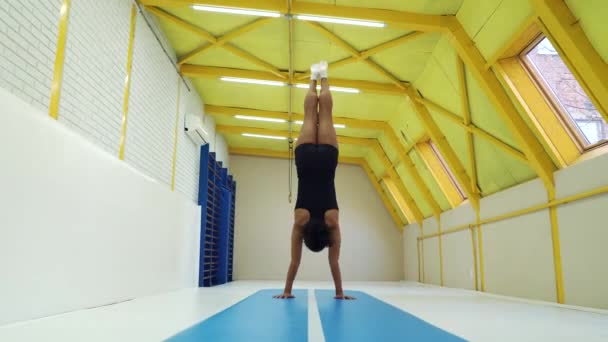 Девушка-акробатка делает стойки на руках и переворачивает коврики в спортзале — стоковое видео