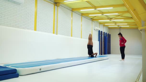 Personal trainer showing handstands and flips on mat in gym — Stockvideo