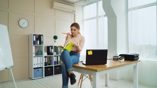 Молодая деловая женщина сидит на рабочем столе и пишет в блокноте — стоковое видео