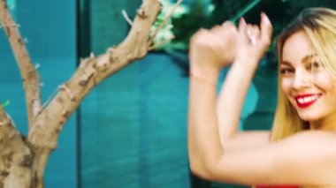 portrait of cheerful blonde woman looking at camera and dancing on street