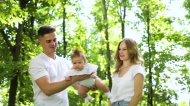 Yeni doğmuş bebeğiyle sevgi dolu bir aile güneşli bir bahçede vakit geçiriyor.