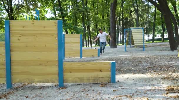 Cheerful man training Jack Russell Terrier to jump over barrier on playground — Stock Video