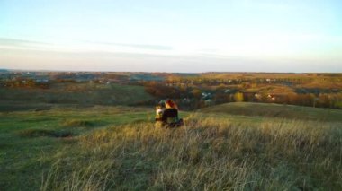 Owner and pet American Staffordshire terrier sitting on green hill at sunset