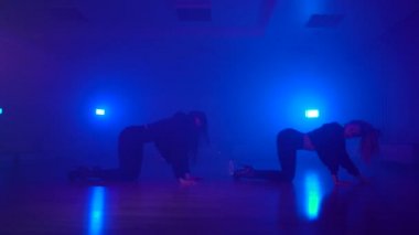 Sexy girls dancing in duo on floor in dark studio with fog and neon lights
