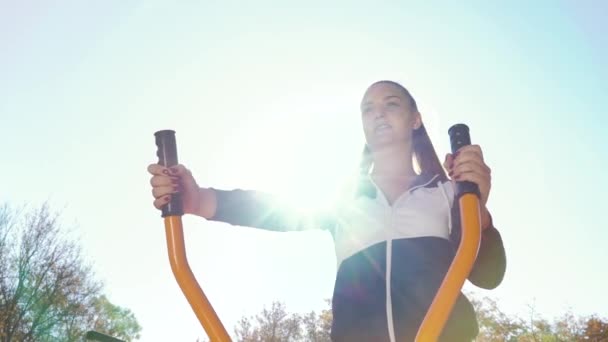 Young pretty girl training on exercise bike on sunny day outside — Stock video