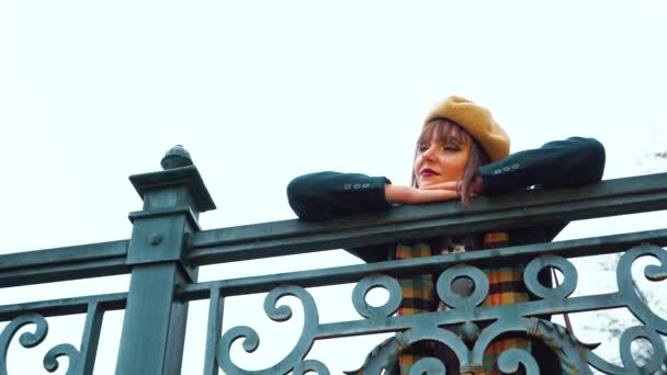 Pensive girl wearing beret and coat posing on metal bridge — 图库视频影像