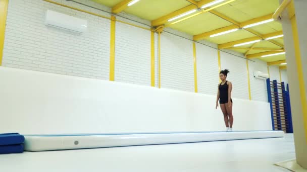 Девушка-акробатка практикует сальто на ковриках в спортзале — стоковое видео