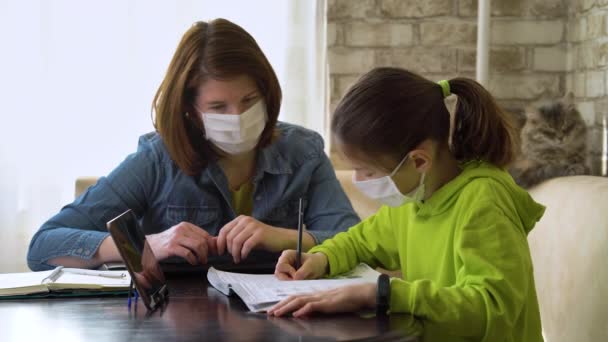 Anya és lánya orvosi maszkban, együtt csinálják a házi feladatot. — Stock videók
