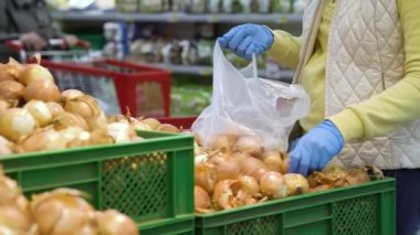 Eldiven giymiş kadın eller markette poşete soğan koyuyor.