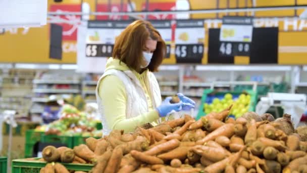 Vrouw met masker koopt wortelen in de supermarkt tijdens de pandemie — Stockvideo