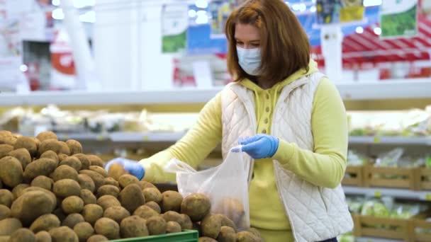 세계적으로 유행하는 식료품 가게에서 감자를 줍고 있는 마스크를 쓴 젊은 여자 — 비디오