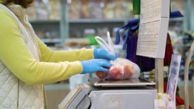 Tıbbi eldivenli kadın bakkalda elmaları tartıyor.